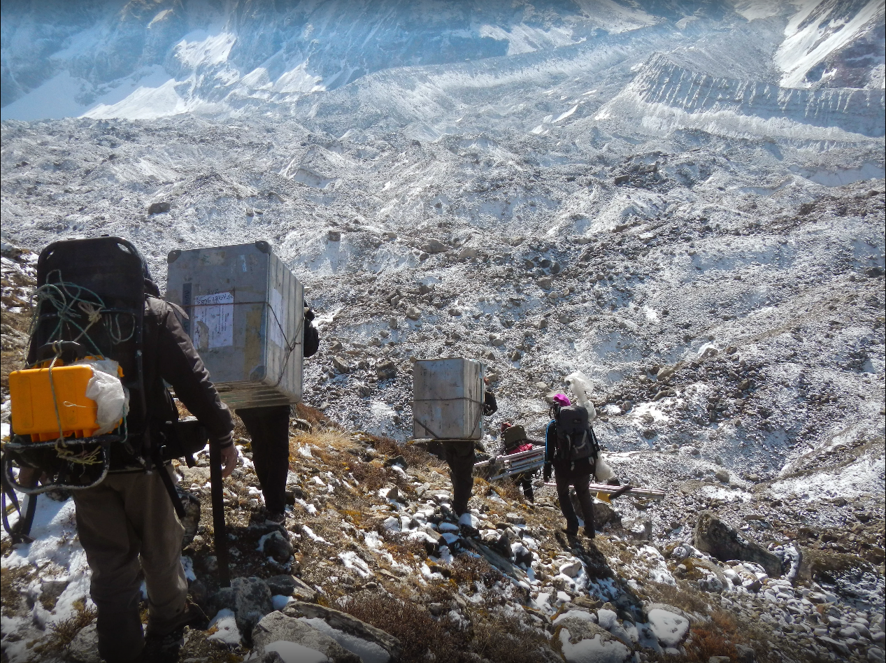 Personas caminando en un glaciar con cargamentos a la espalda