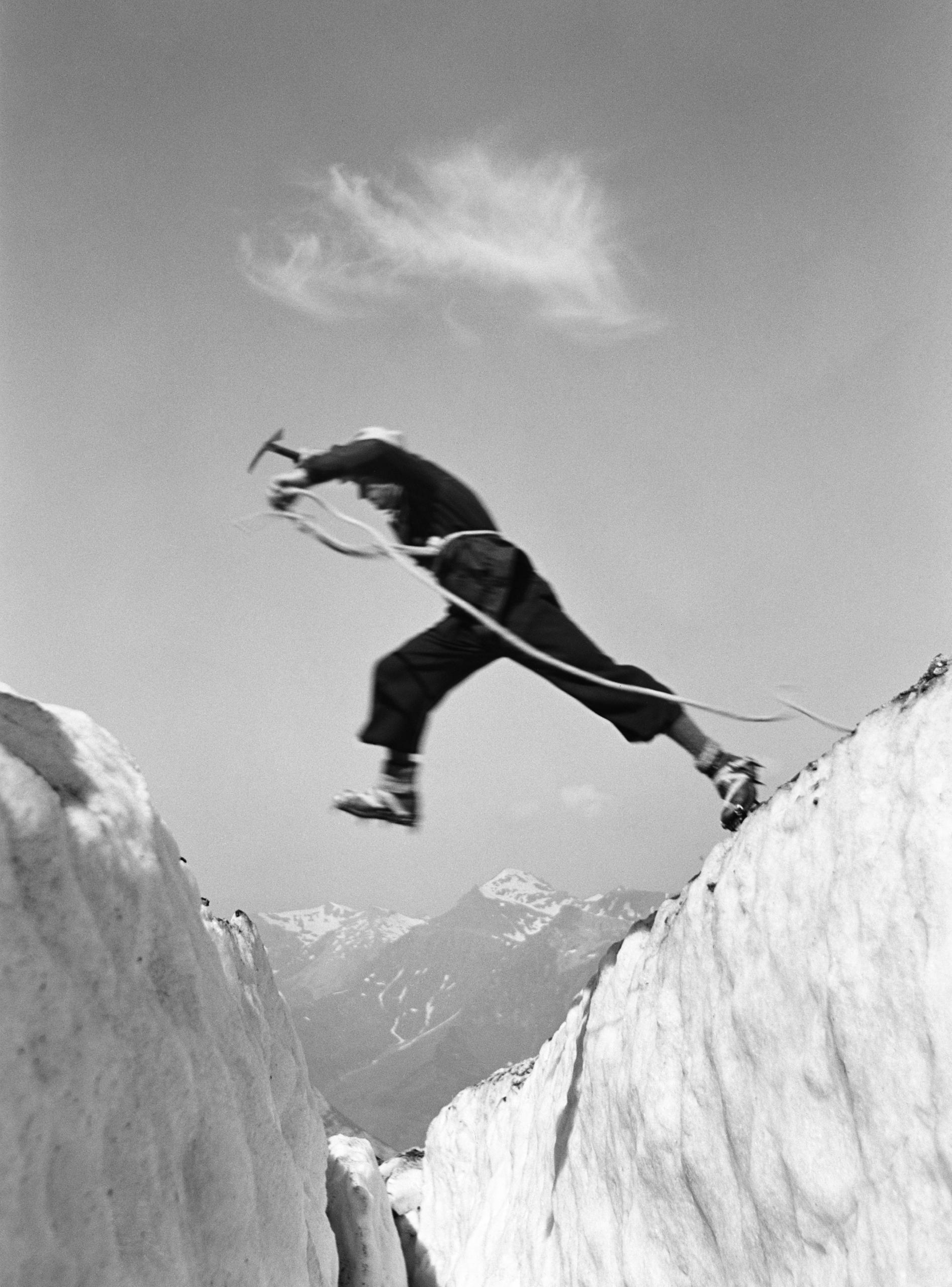 صورة بالأبيض والأسود لقفزة يقوم بها رجل عبر شق جليدي في منطقة جبلية