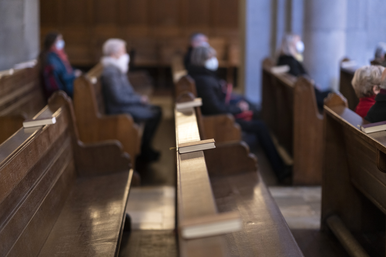 Panche vuote di una chiesa e acuni fedeli seduti in sottofondo