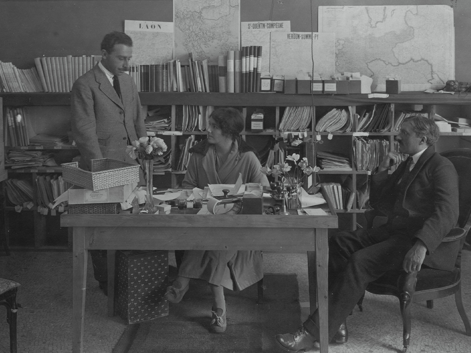 Frau an einem Schreibtisch, umgeben von Männern