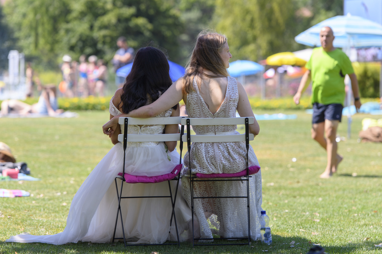 Due donne vestite da sposa sedute su due sedie in un parco fotografate di spalle