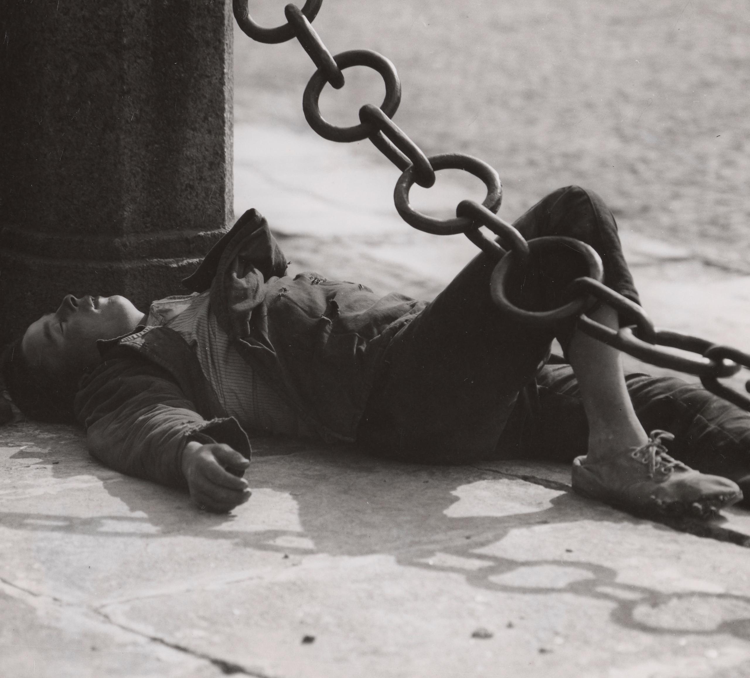 صورة بالأبيض والأسود لطفل نائم في الشارع وفوقه سلسلة حديدية