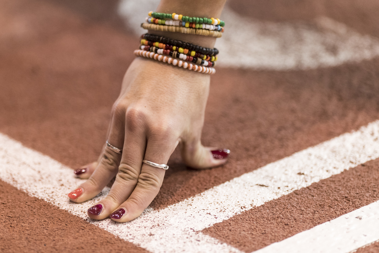mano di atleta donna con unghie dipinte e numerosi braccialetti appoggiata sulla pista, pronta a partire