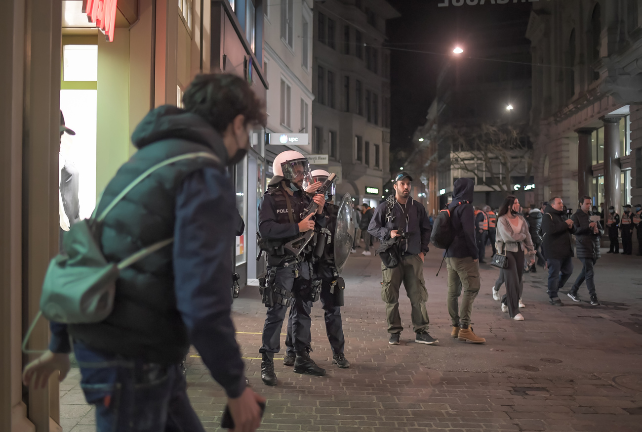 persone attorno a poliziotti in assetto antisommossa