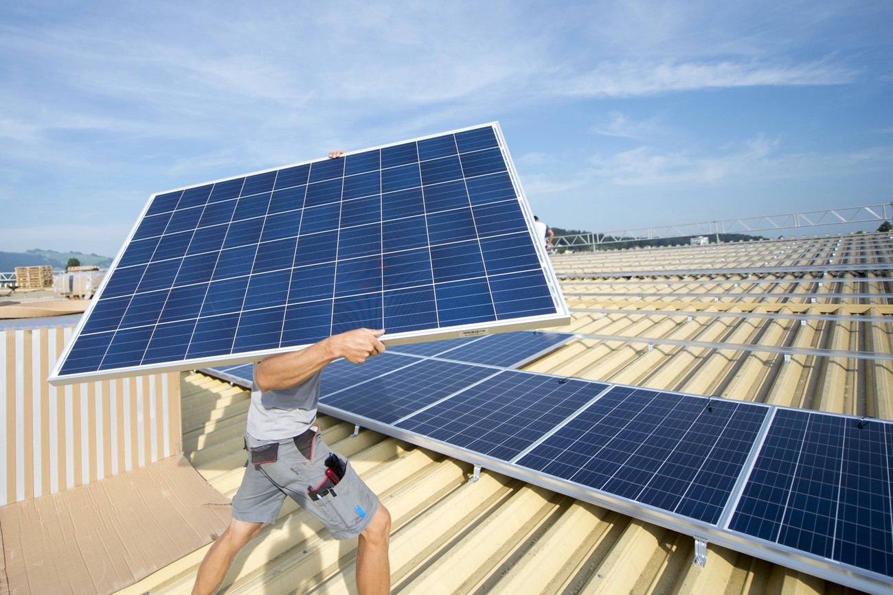 Ein Mann trägt ein Solarmodul auf ein Dach