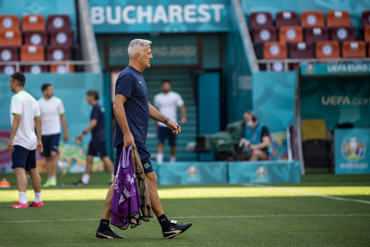 Uomo con capelli grigi cammina su campo da calcio portando maglie viola nella mano destra