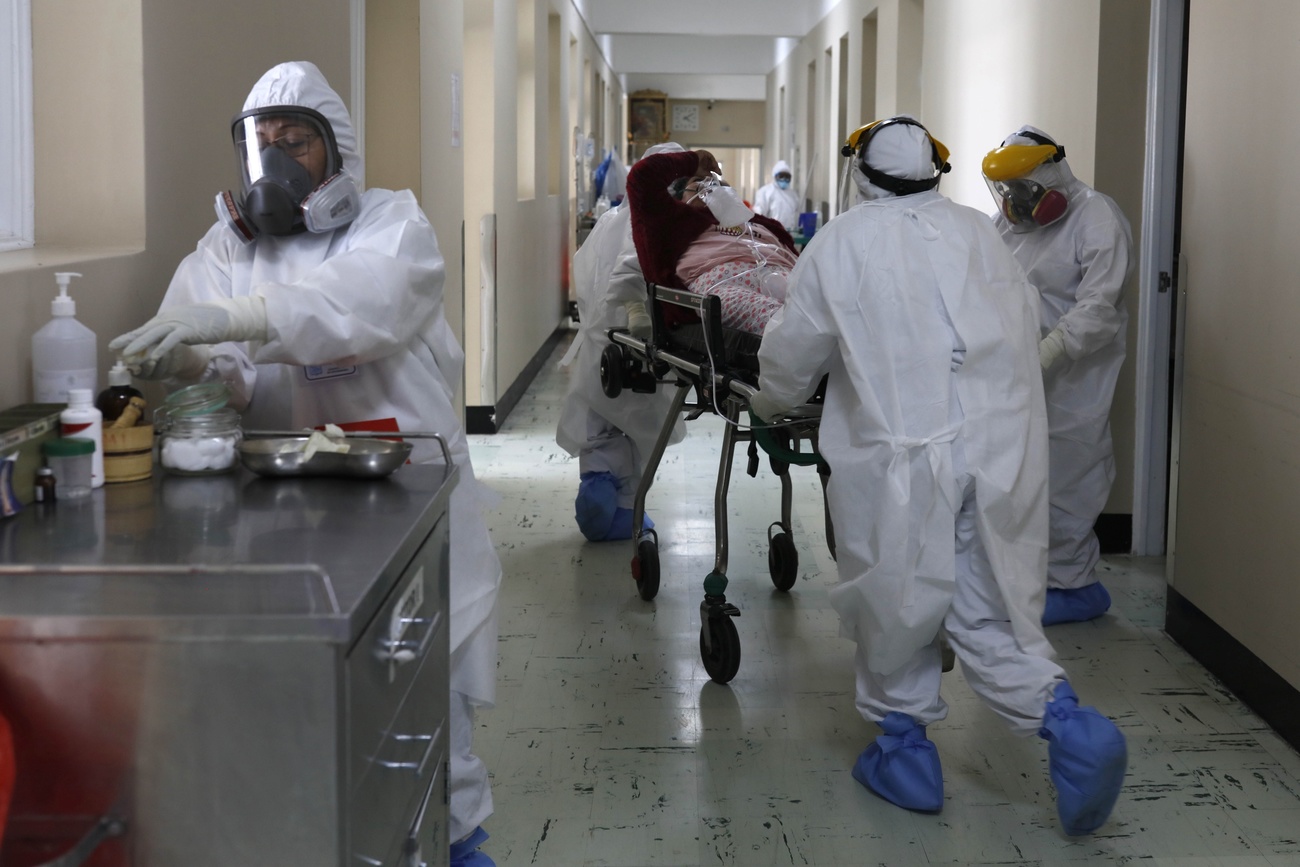 Tre persone in protezione completa e maschere a gas, due di loro spingono un pazientesu un lettino in un corridoio d ospedale