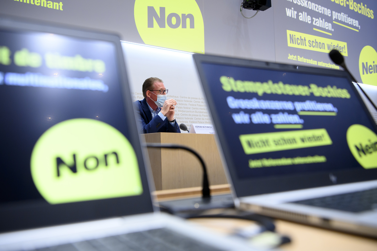 Two computer screens with campaign logos and a panel speaker in the background