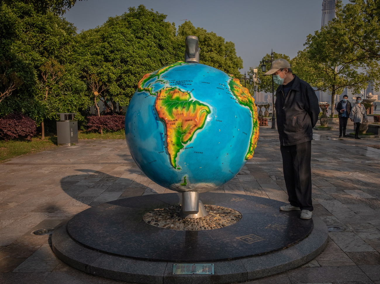 Un uomo con la mascherina chirurgica osserva da vicino un mappamondo.