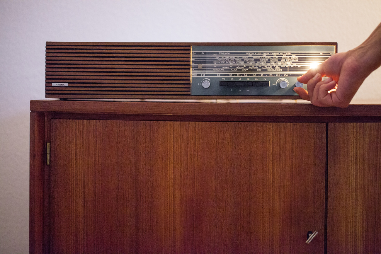 old radio on a wooden piece of furniture and a hand moving the knob looking for a radio frequency