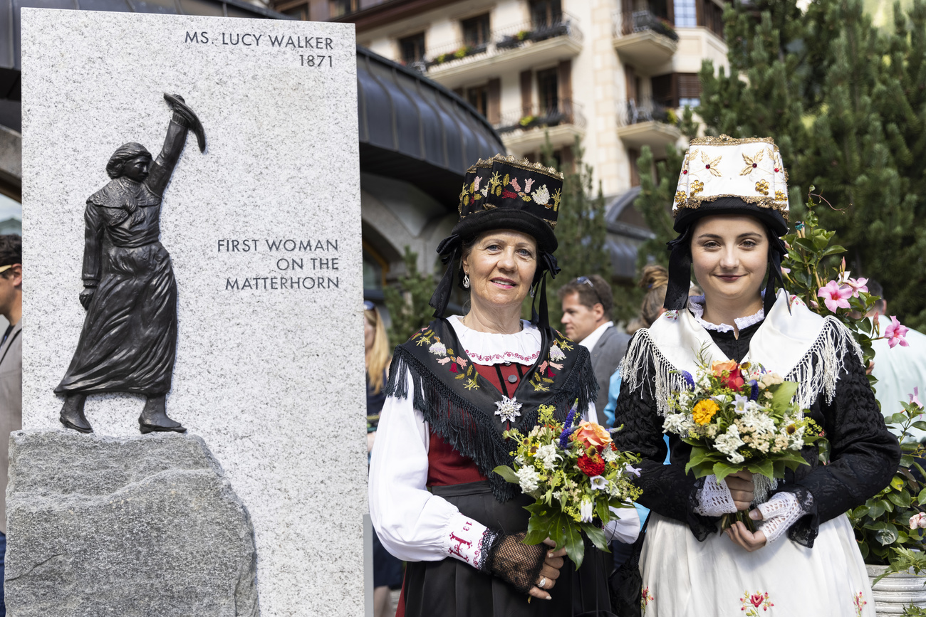 Dos mujeres con trajes tradicinales posando junto a una escultura