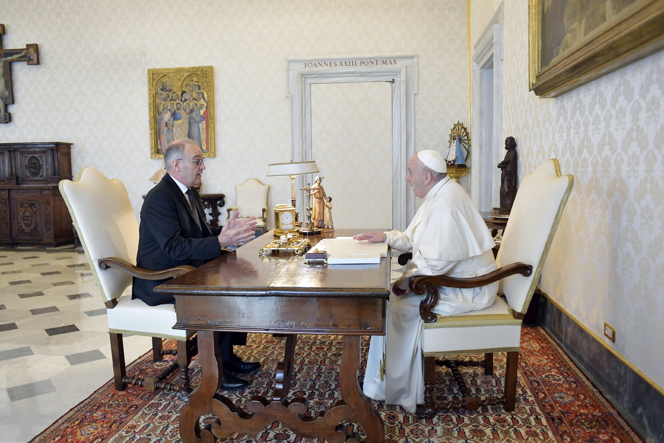 Un homme en costume assis avec le pape à un bureau.