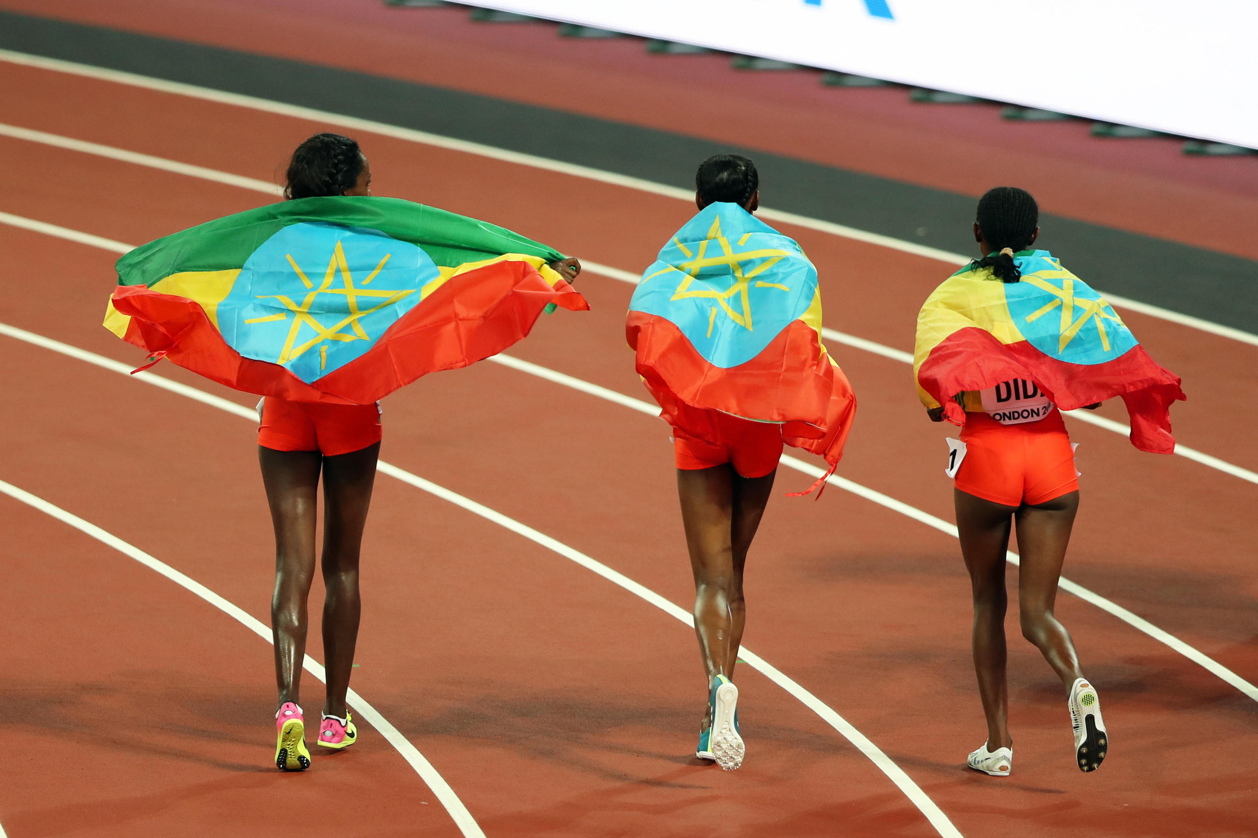 Trois athlètes enveloppées d un drapeau dans un stade.