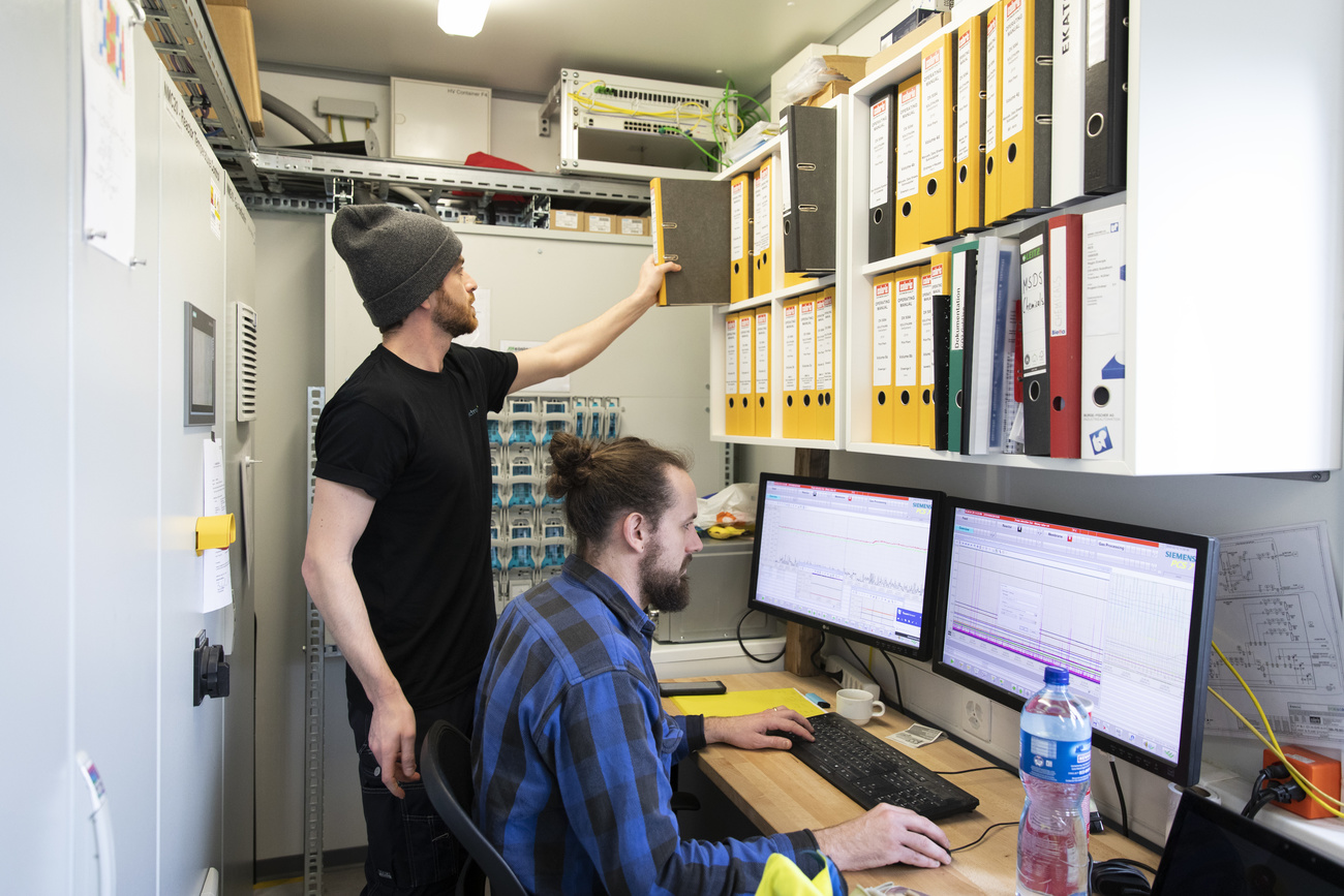 An engineer and a scientist in an office with computers and bookshelf