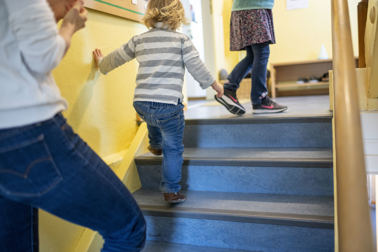 bambino di 2-3 anni fotografato di schiena mentre sale le scale appoggiandosi al muro con la mano sinistra