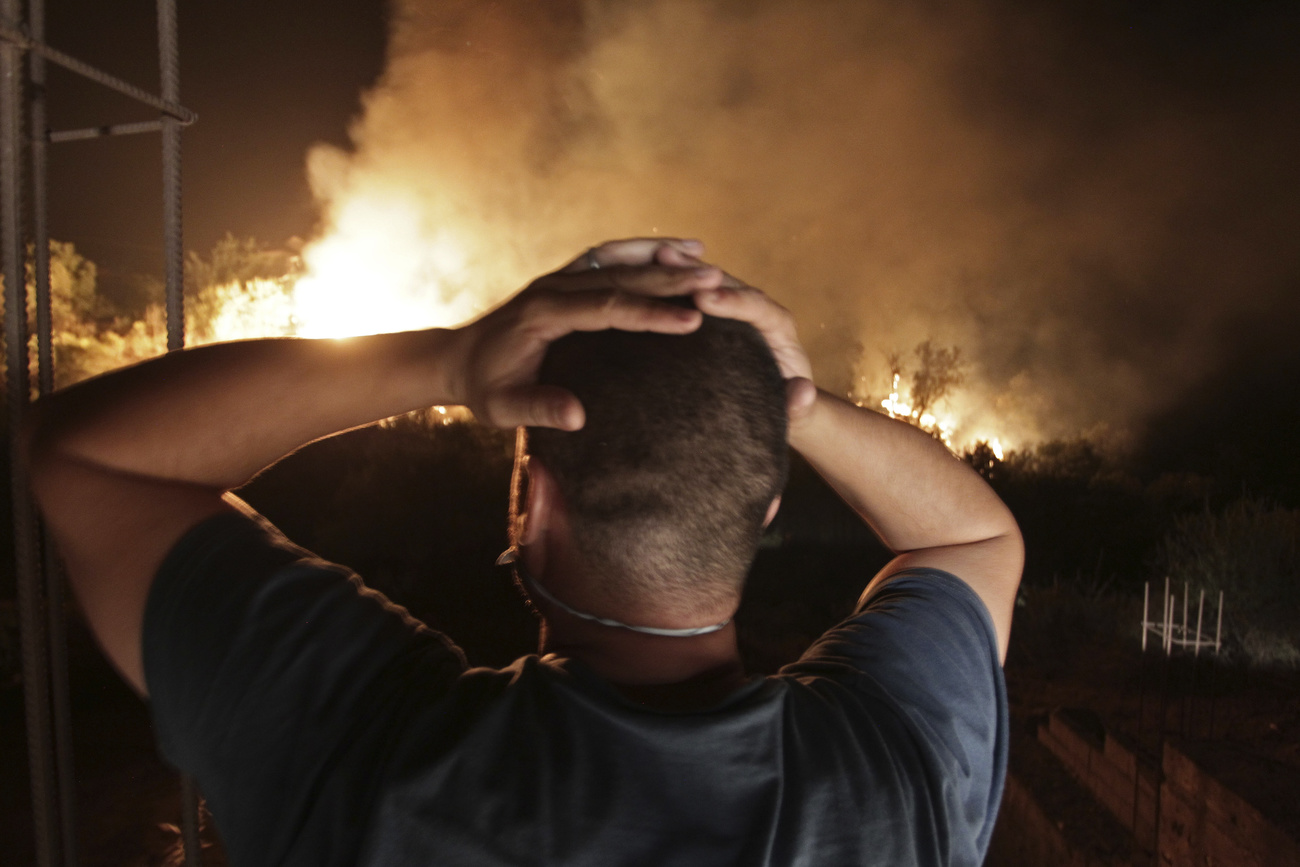 uomo fotografato di spalle si tiene la testa con le mani osservandoun incendio