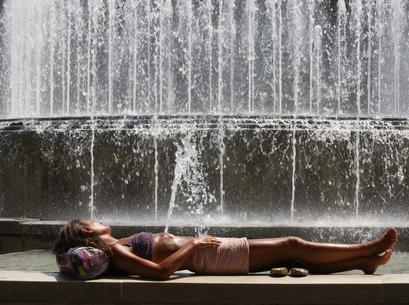 Donna sdraiata su una panchina con dietro una fontana.