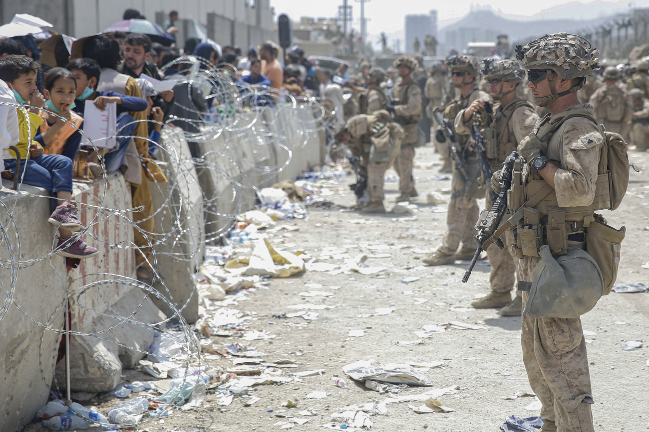 soldati osservano folla dietro a una barriera di filo spinato