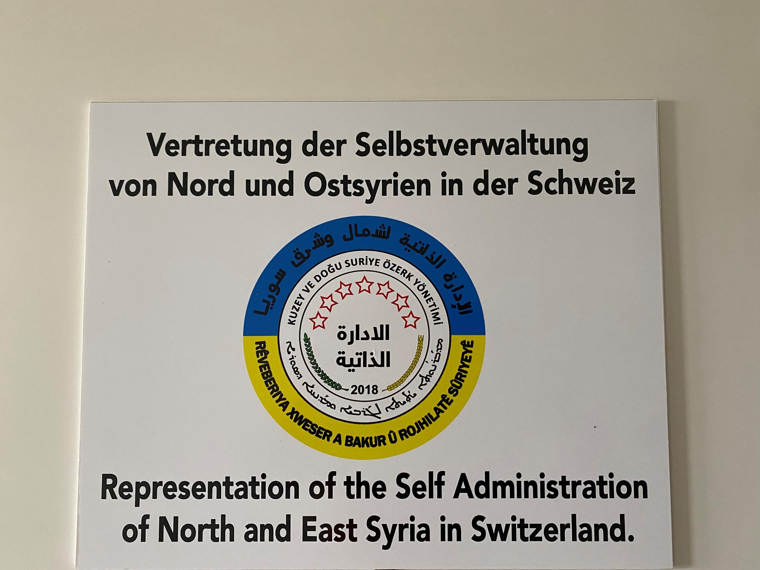 شعارٌ مثبت على جدار مكتب افتتحته الإدارة الذاتية لشمال وشرق سوريا في مدينة جنيف