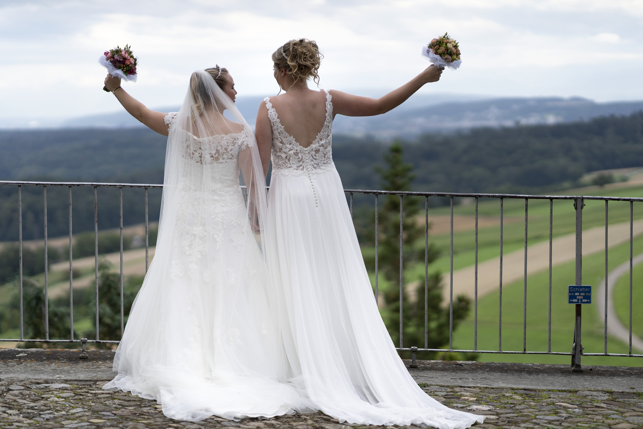 Two women on a bridge in white wedding dresses and bouquets of flower