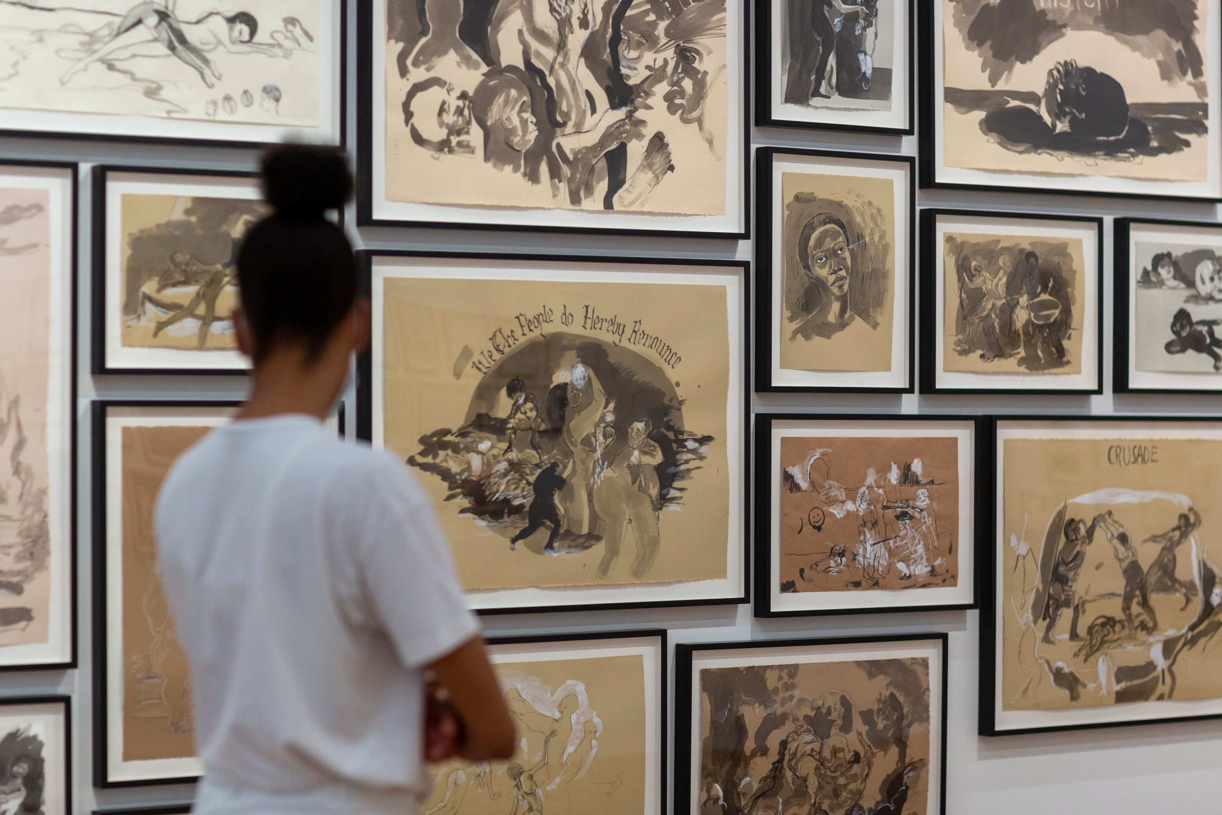 Femme noire regardant des tableaux accrochés à un mur.