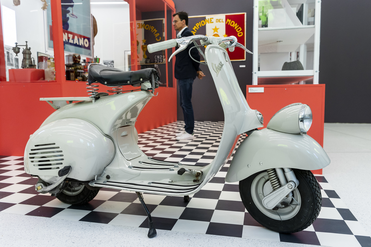 vespa in primo piano e persona che osserva oggetti esposti in vetrina