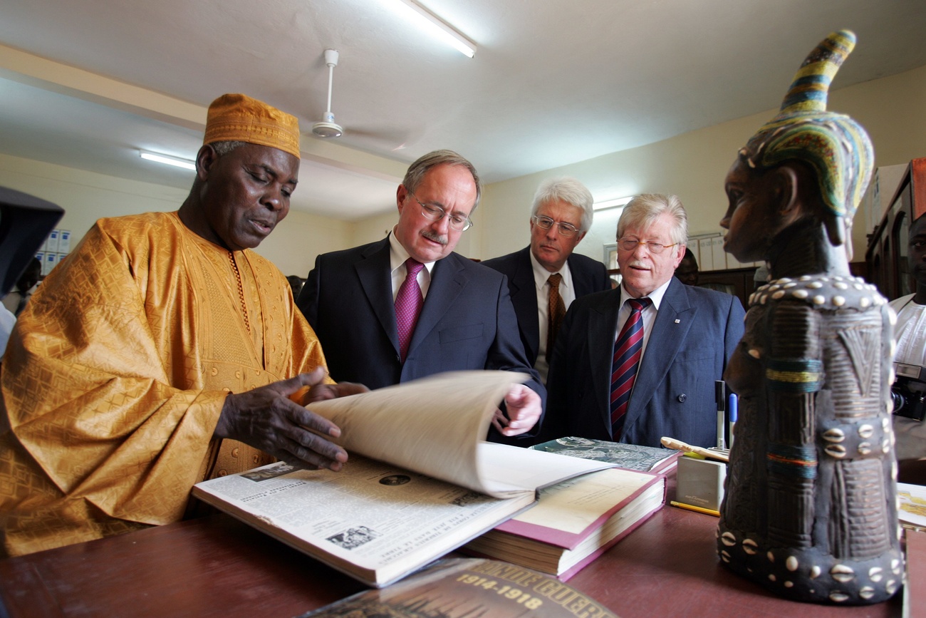 Un groupe d homme autour d un livre et d une statue africaine.