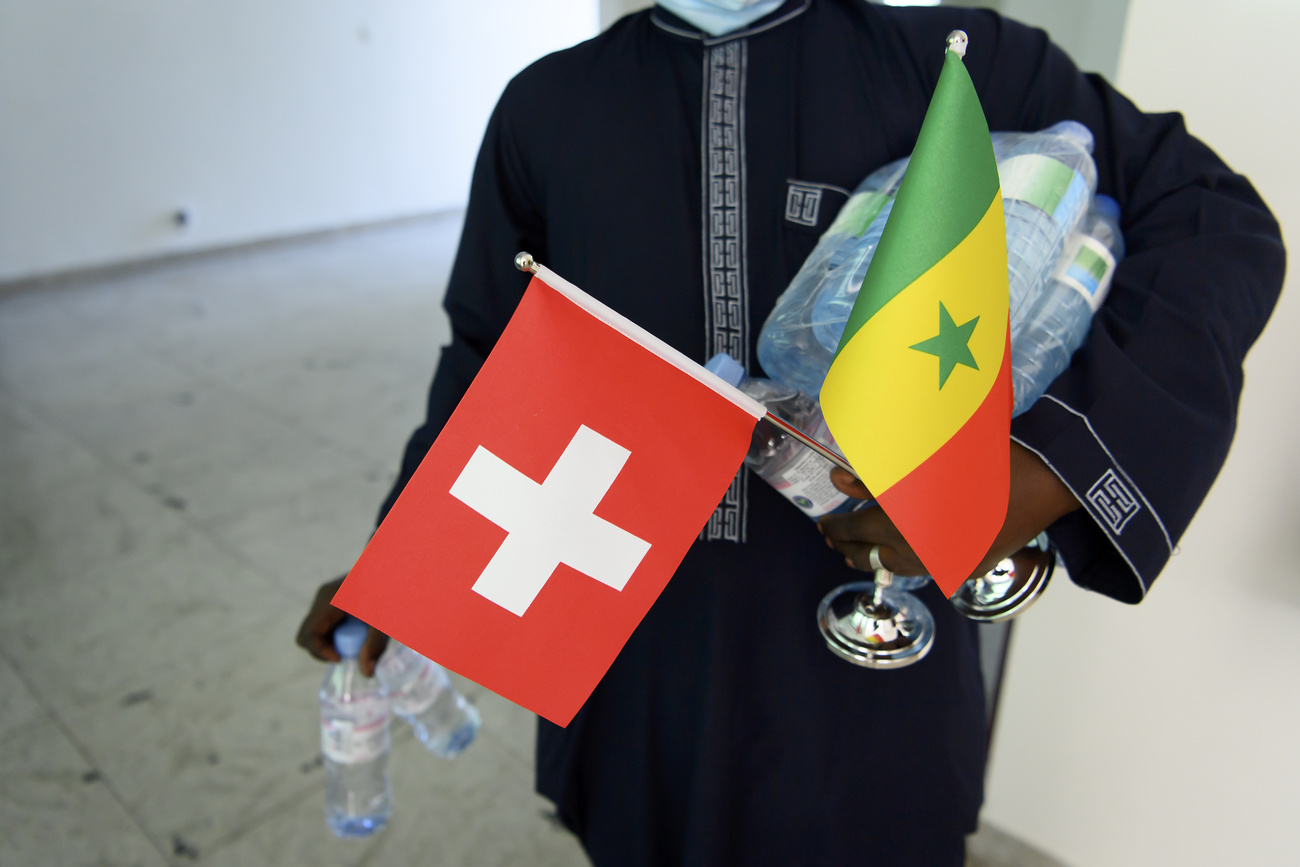 Boy carries water bottles and Swiss and Senegal flags