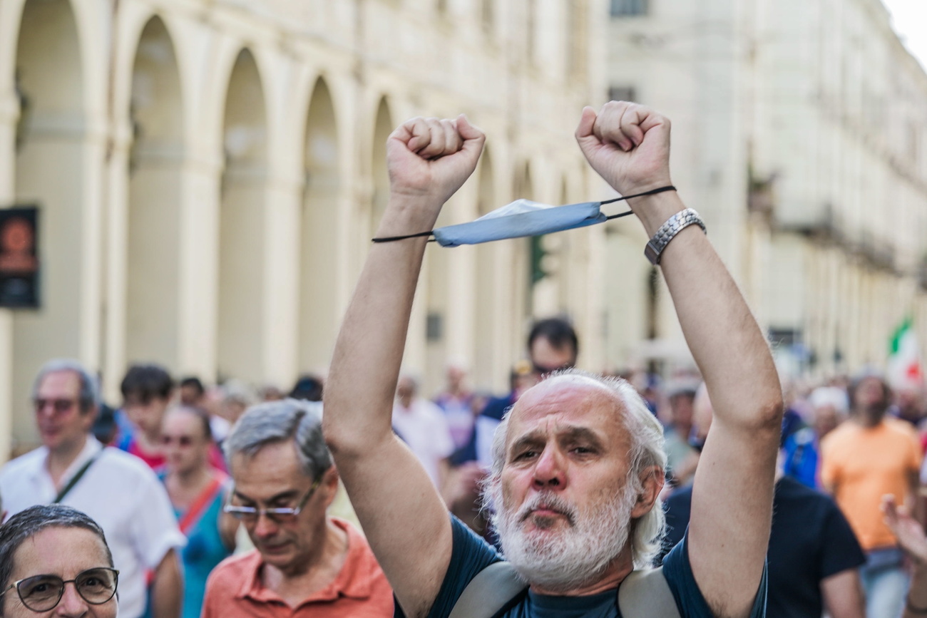 uomo con barba bianca in folla che protesta. usa una mascherina a mo di manette