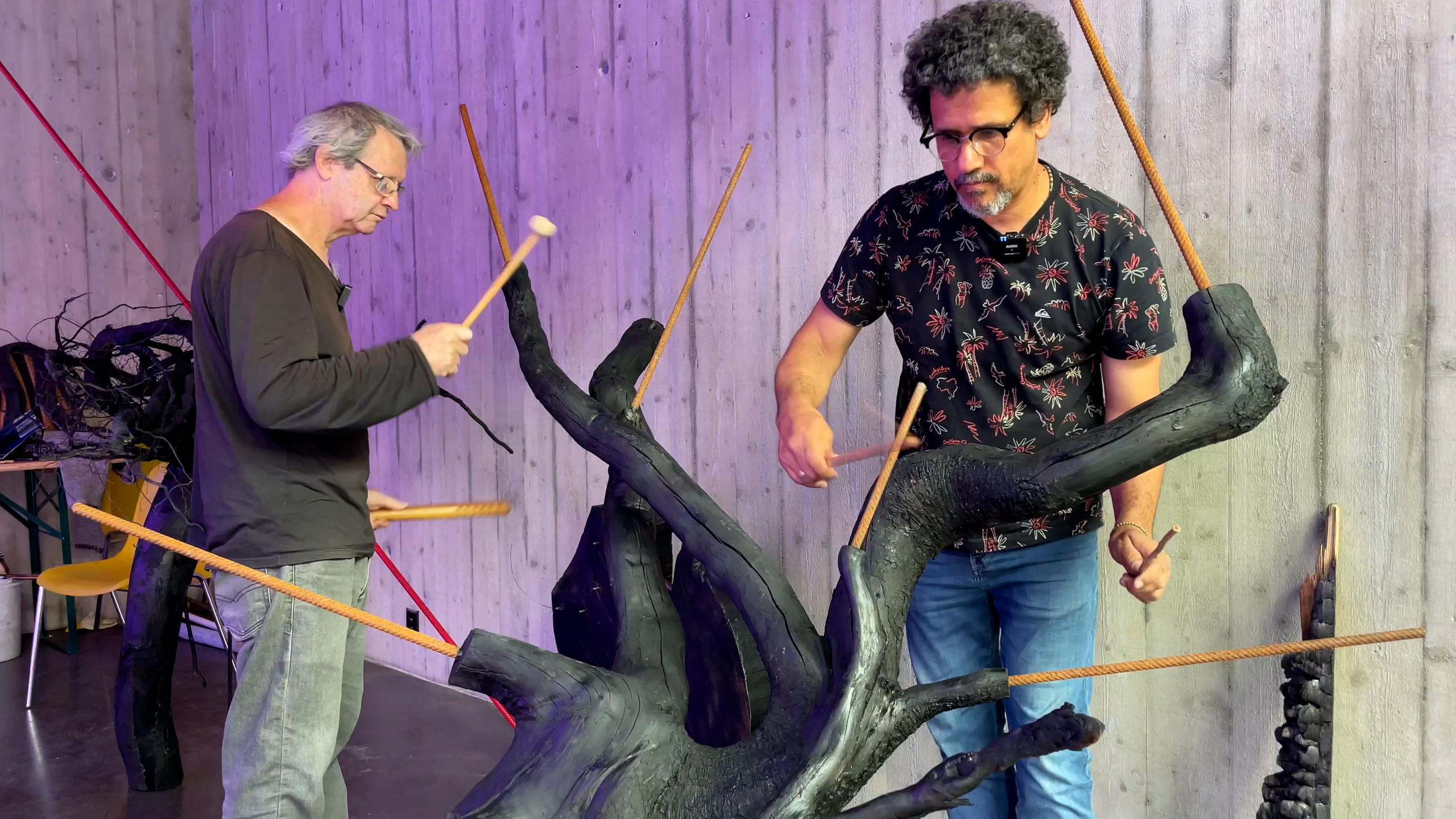 Due uomini con bacchetta da percussionisti battono su sculture ricavate da alberi