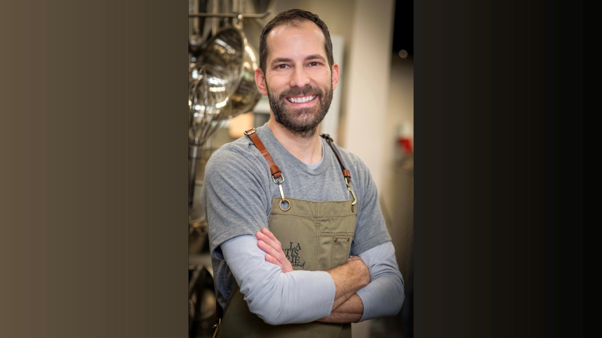 mezzo busto di uomo sorridente con barba e capelli corti con grembiule
