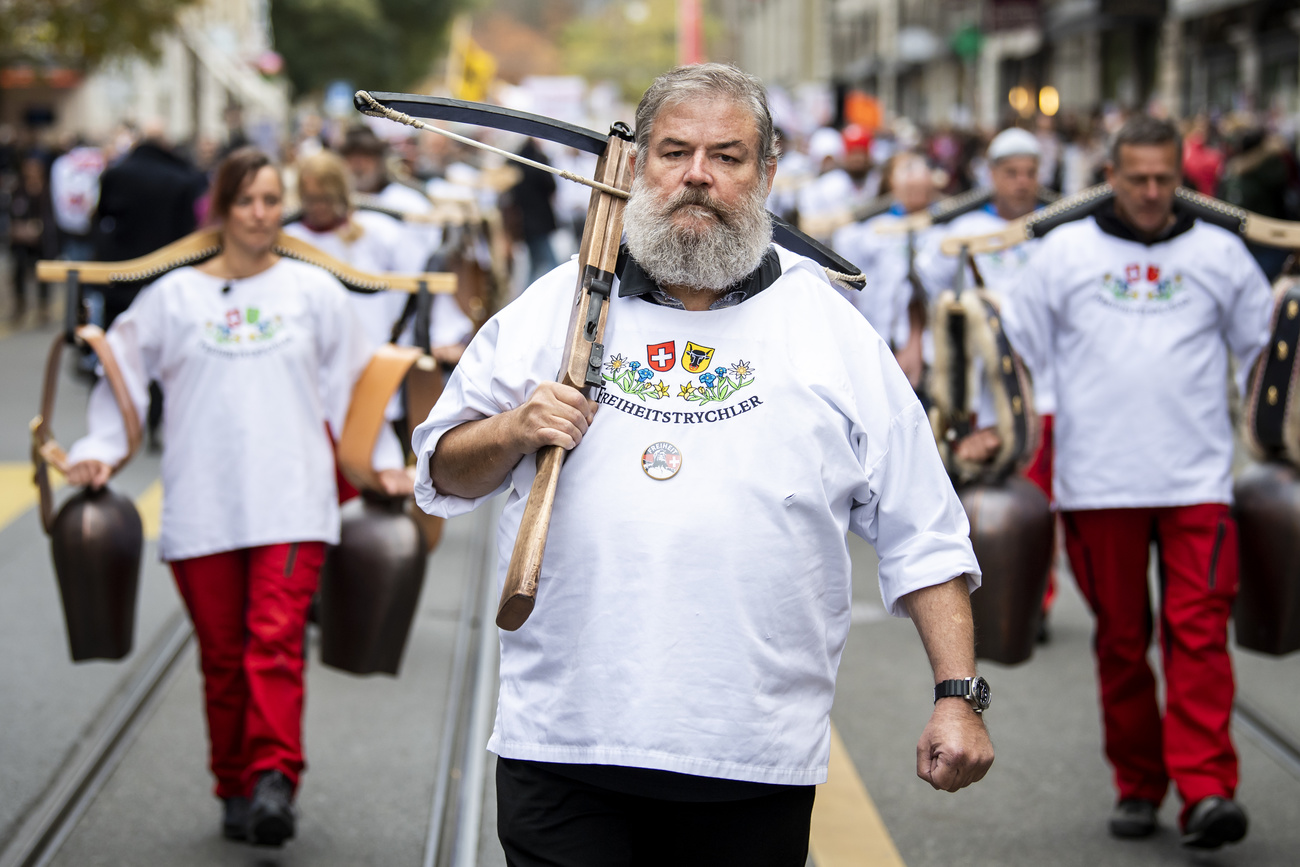 Manifestante con vestimenta típica de Suiza y cencerros. Al frente, un hombre con una ballesta sobre el hombro.