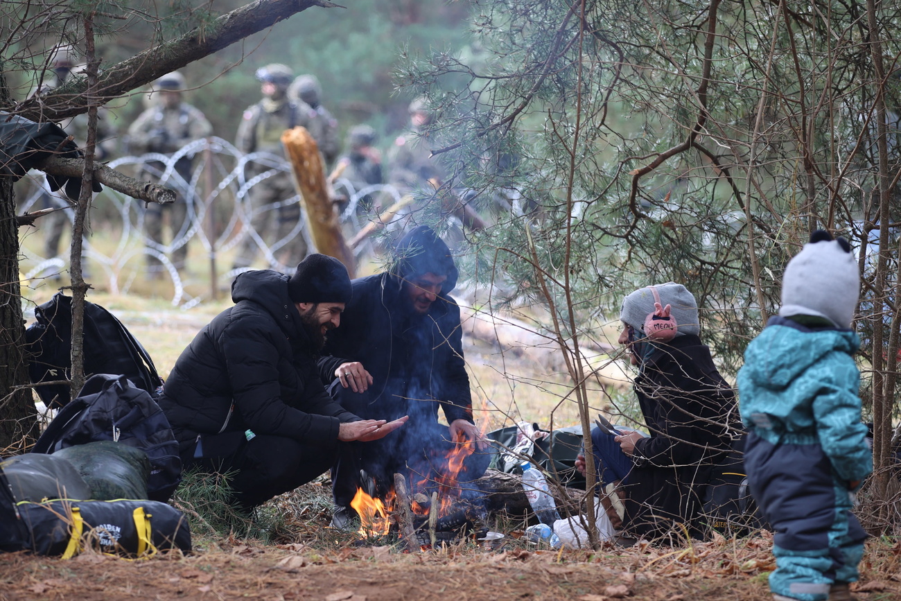 persone cercano di riscaldarsi attorno a un fuoco e in secondo piano militari