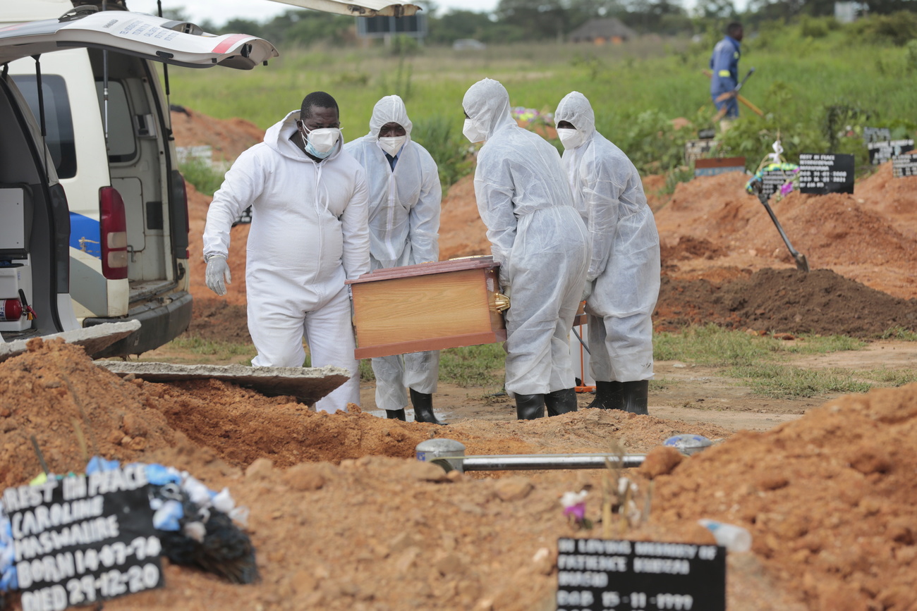 Des employés des services funéraires du Zimbabwe descendent le cercueil d une victime du Covid dans le sol.