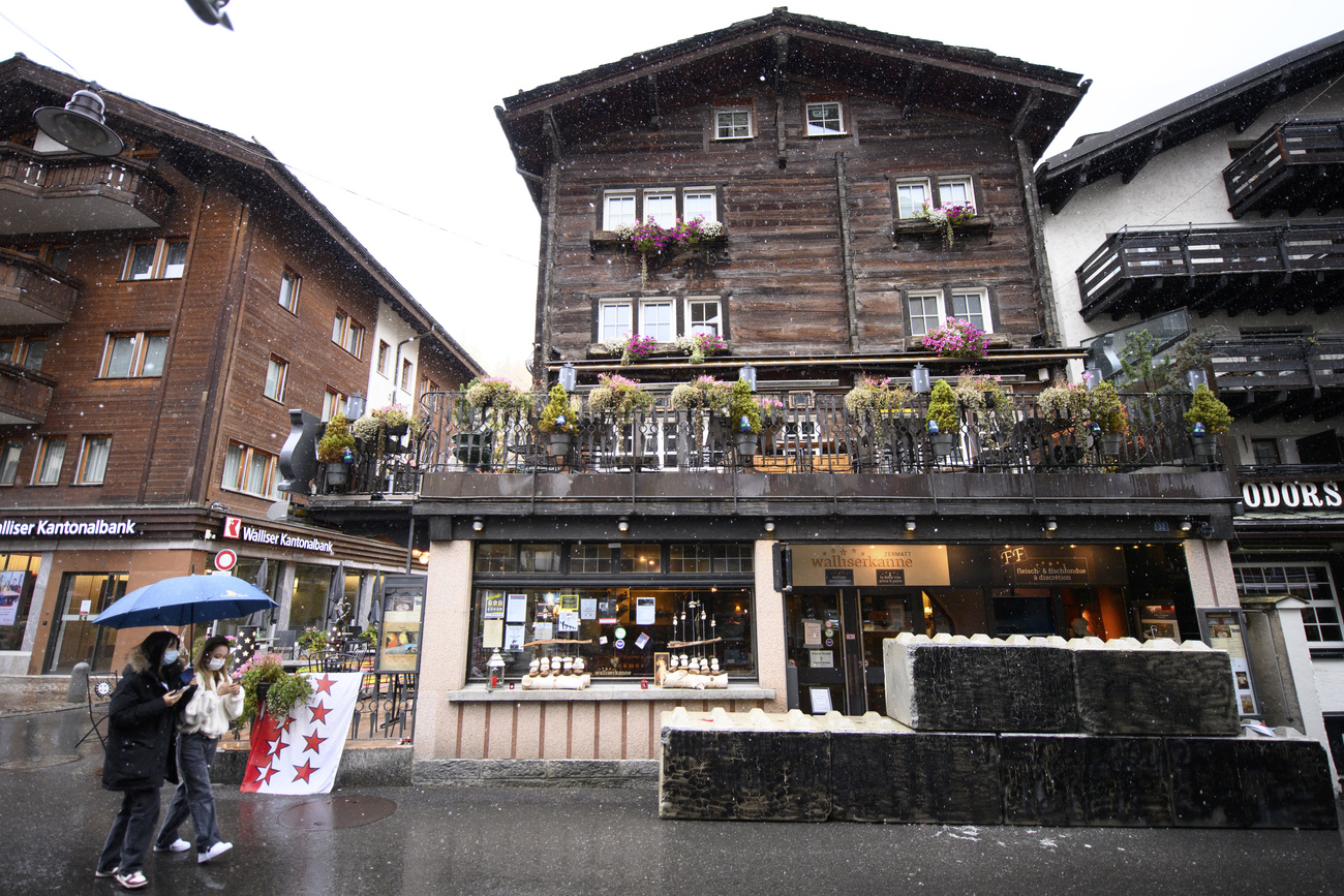 Passersby with umbrellas, and wearing masks, walk past the restaurant
