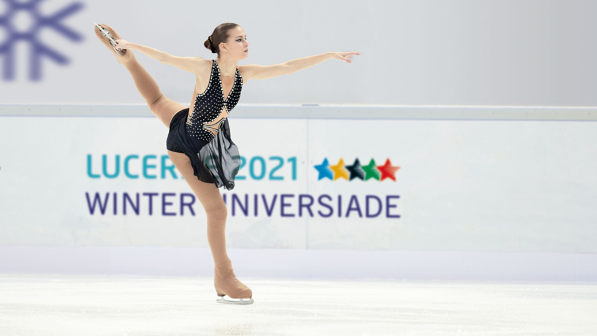 Woman figure skater practices besides a sign for the 2021 Lucerne Winter Universiade