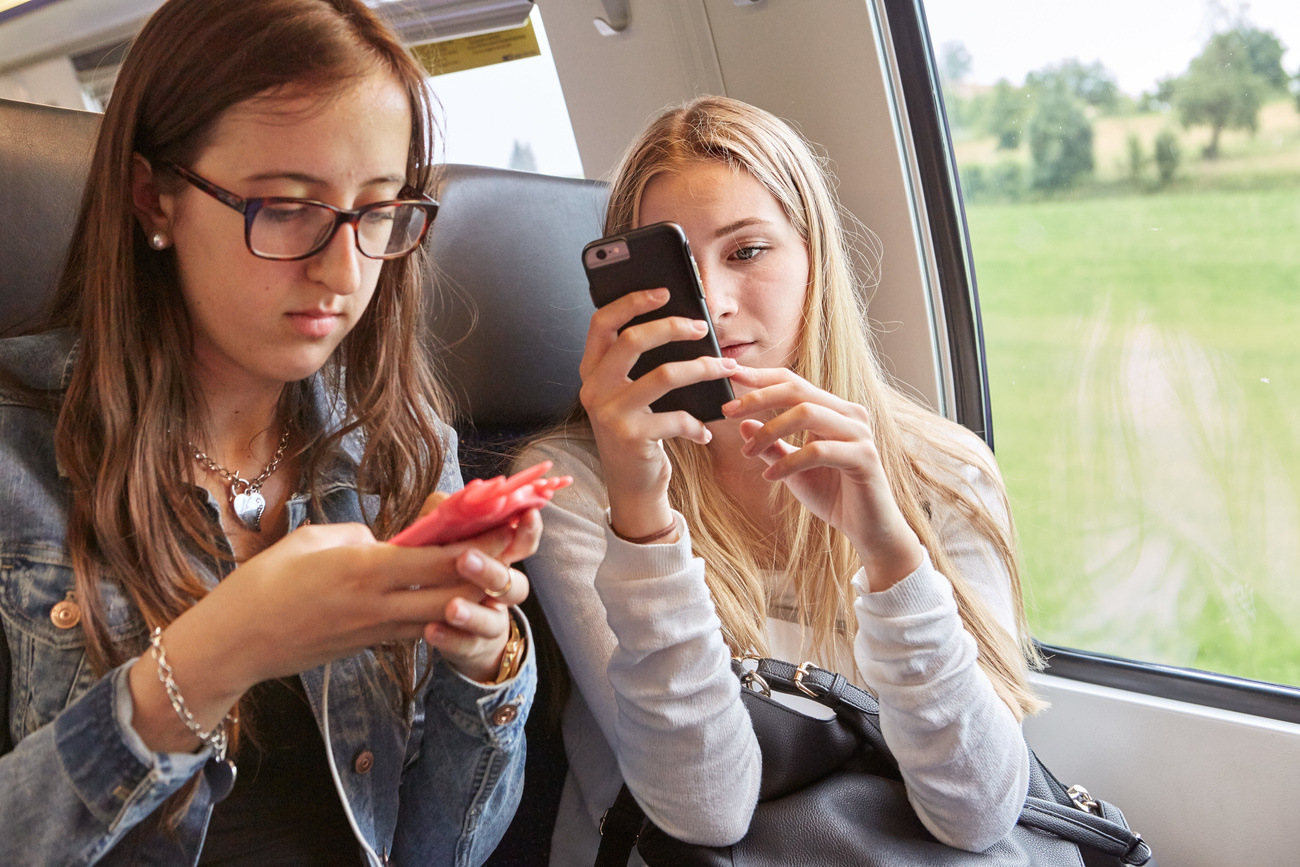 Two young female youths sit on a train looking at smartphones