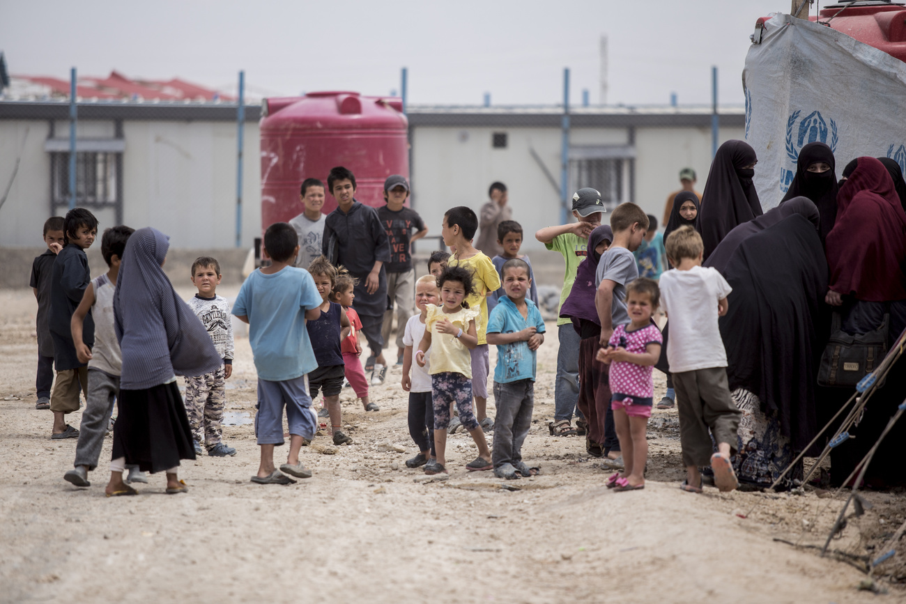 Gruppo di donne e bambini in quello che appare come un campo profughi in zona desertica