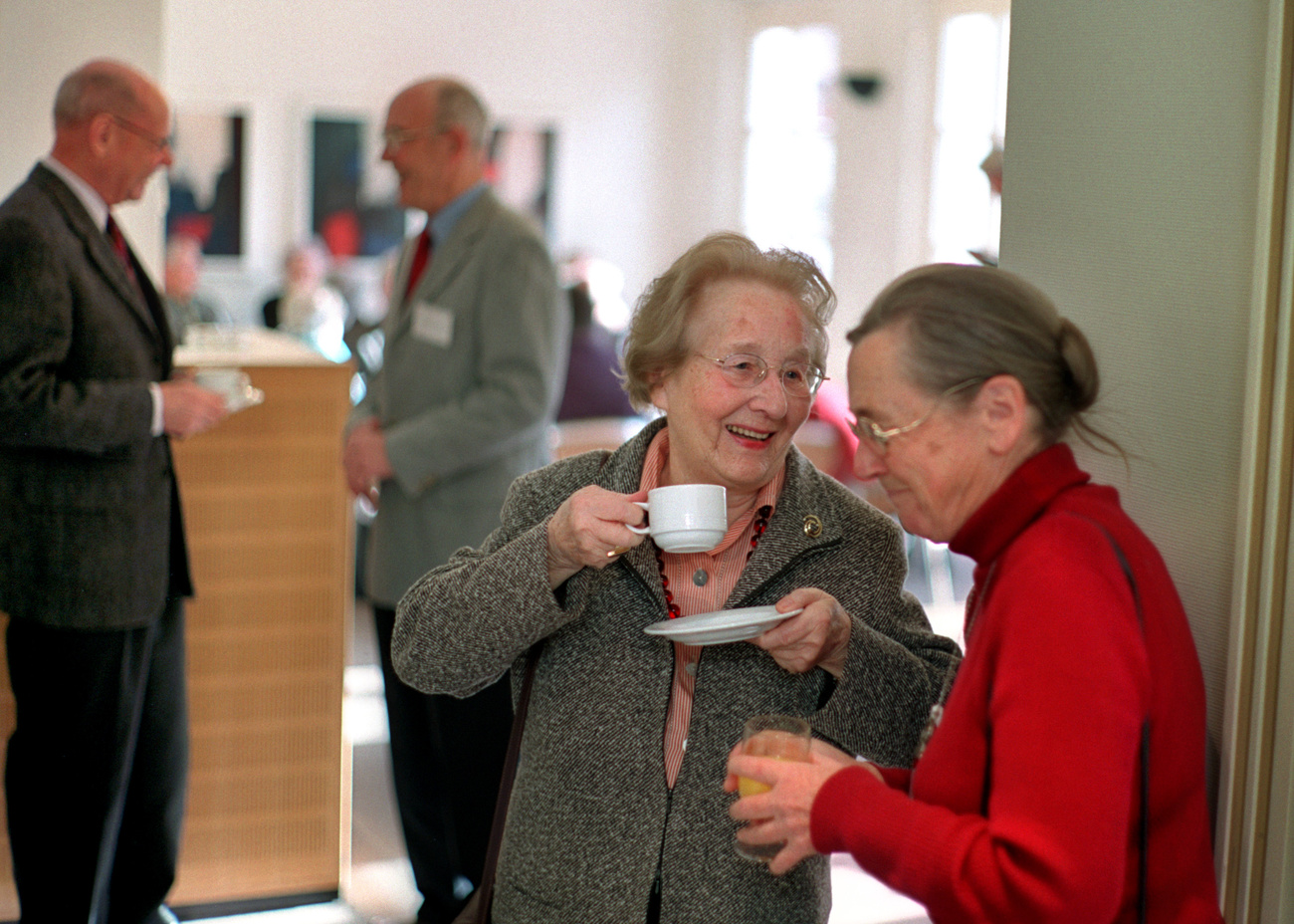 Two elderly women talking, two men in the background