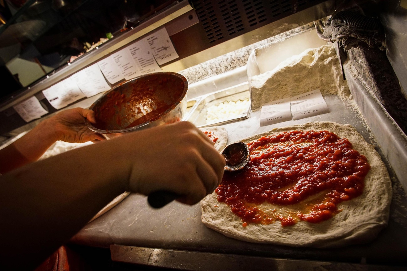 Un pizzaiolo mentre mettere del pomodoro sulla pizza