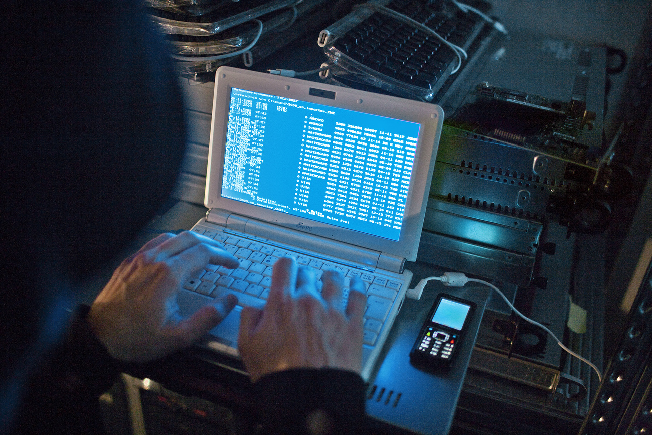 Hooded person using computer in darkened room
