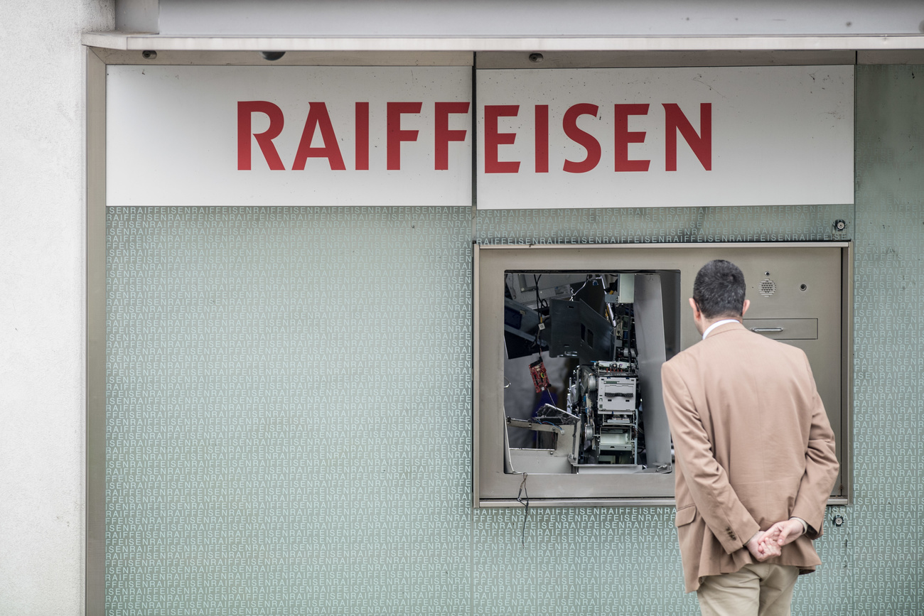 Un uomo guarda un bancomat distrutto da una esplosione.