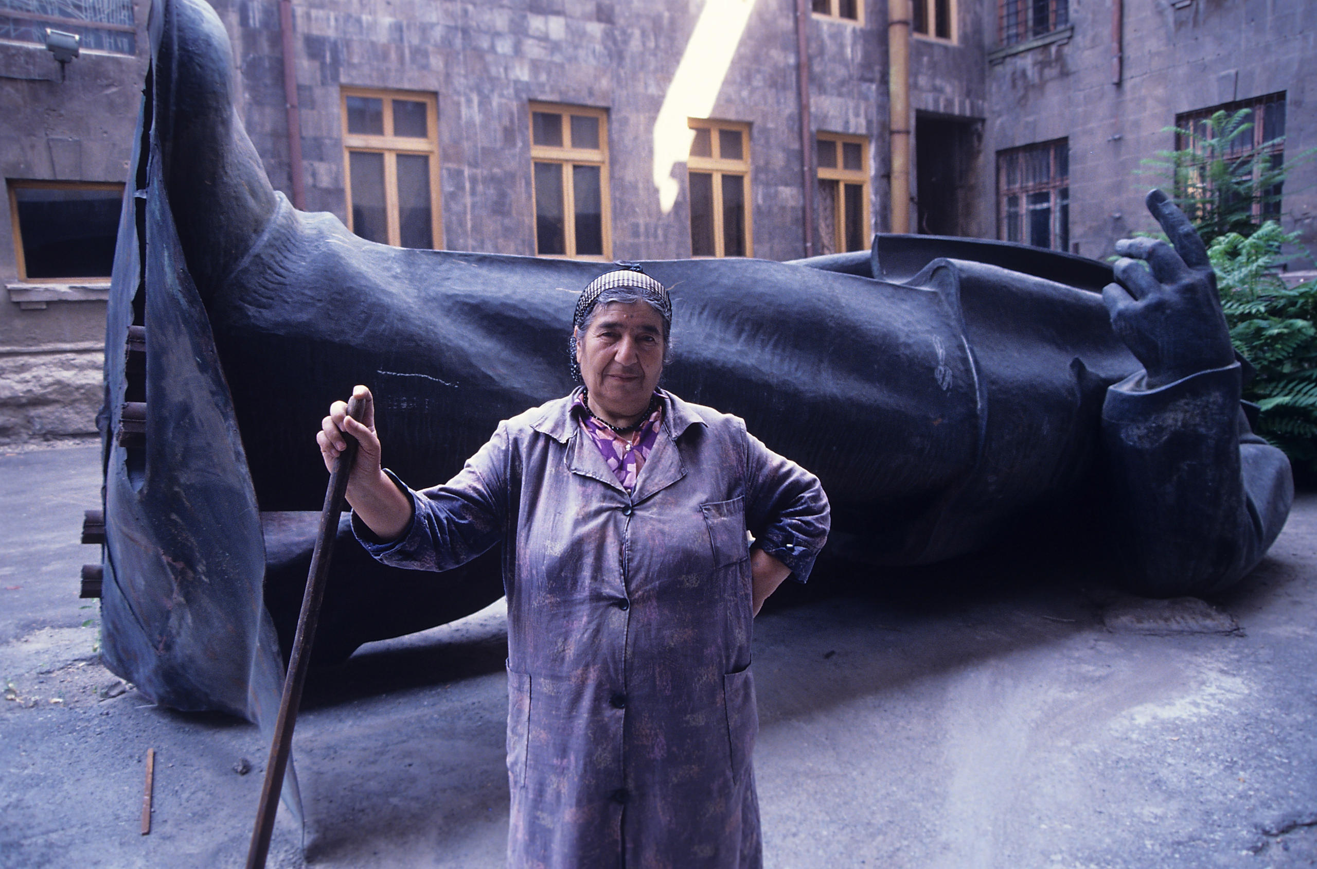 Femme de ménage devant une statue de Lénine à terre.