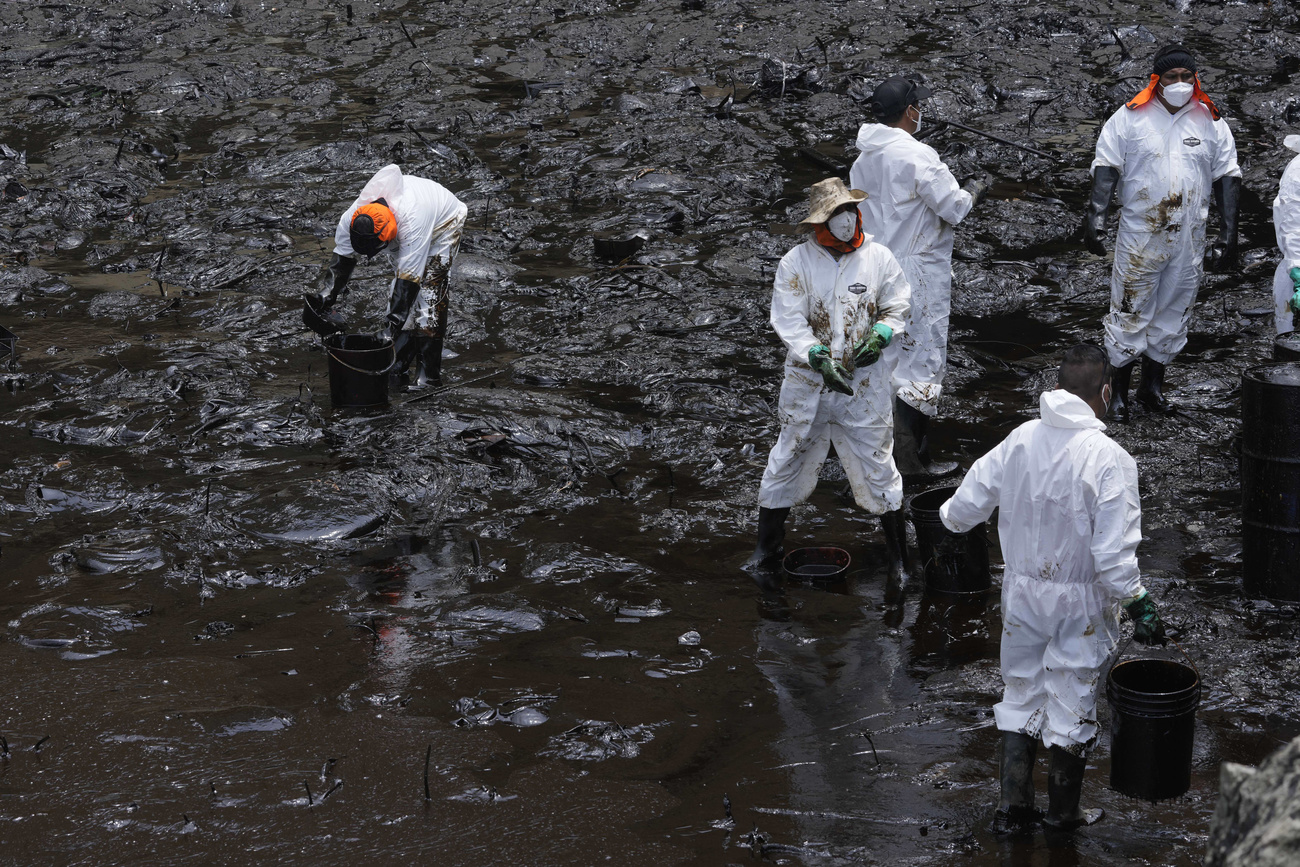 Spiaggia completamente nera dove alcuni operai cercano di eliminare il petrolio.