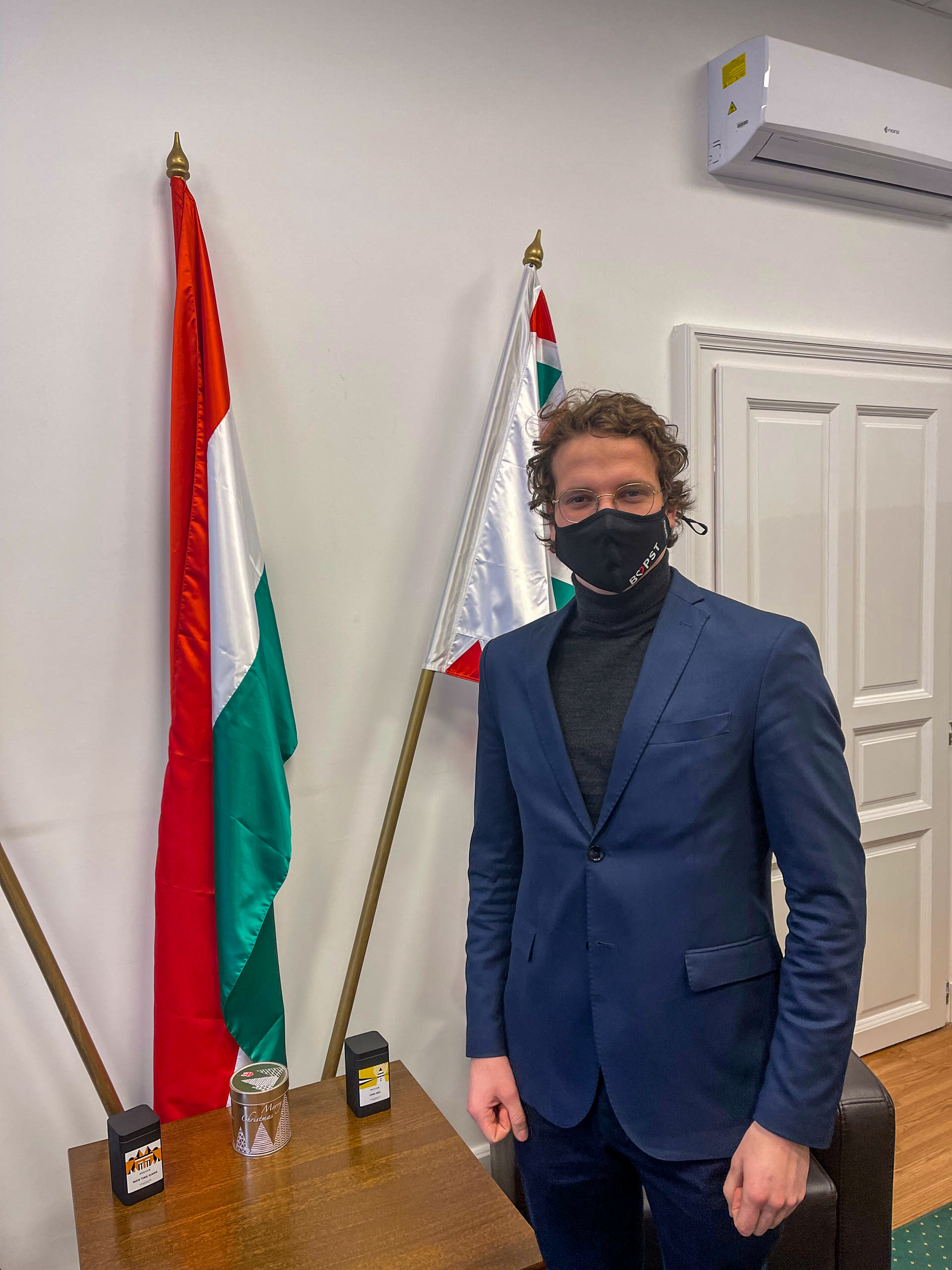 رجل يرتدي قناعا صحيا ويقف بجوار علم المجر