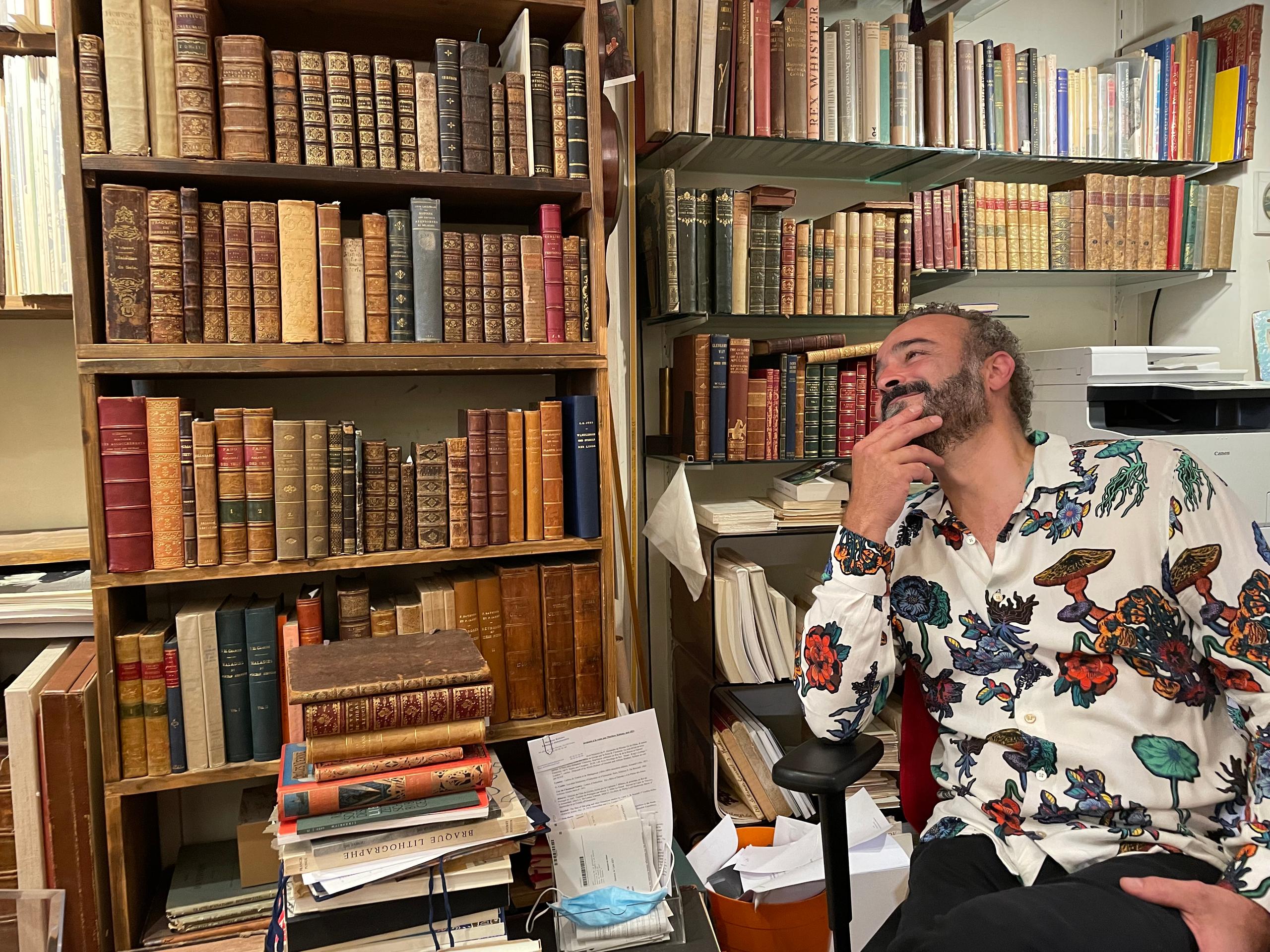 Homme barbu assis dans sa librairie de livres anciens.