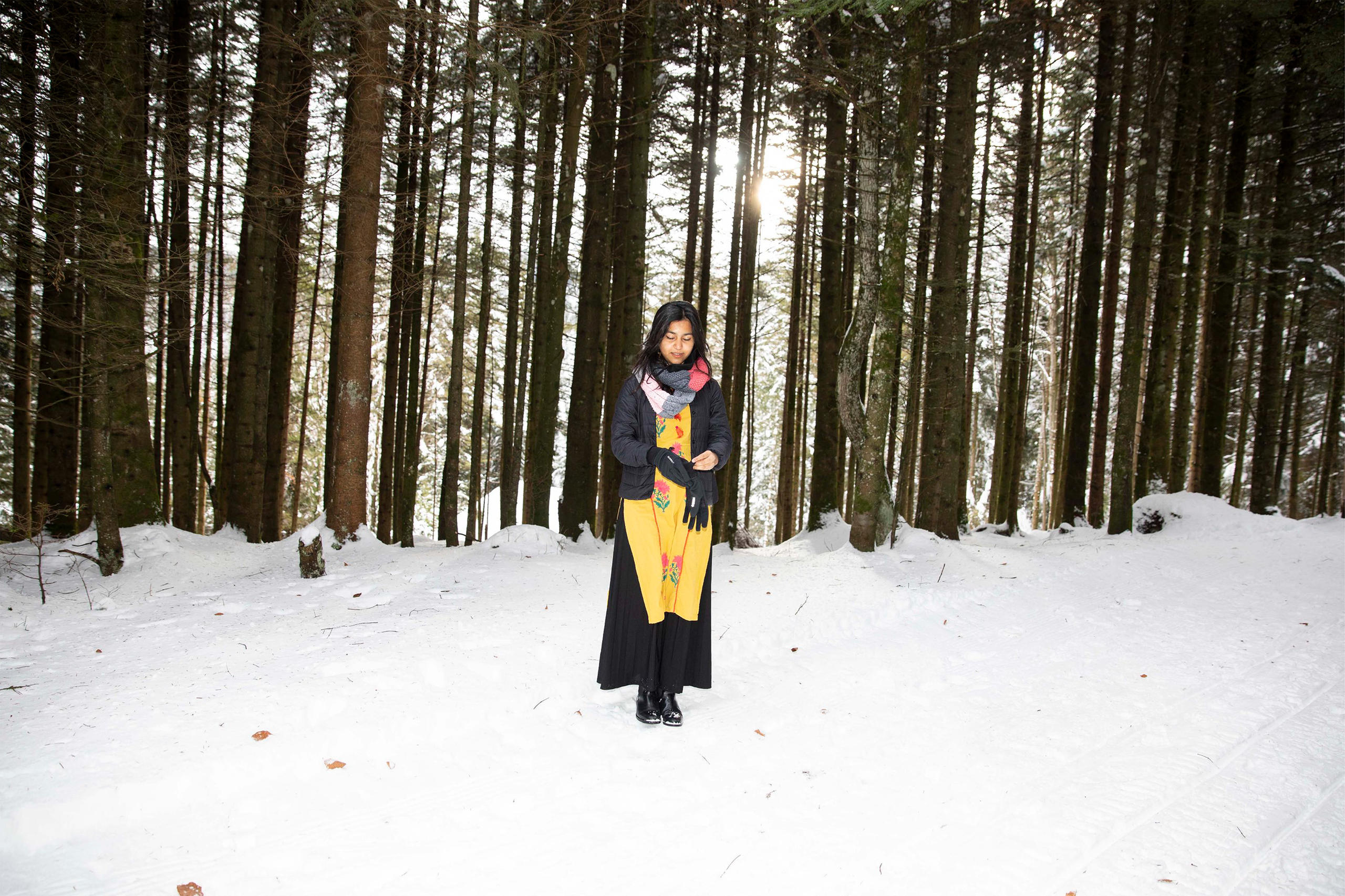 Femme debout dans la neige avec une forêt en arrière-plan.