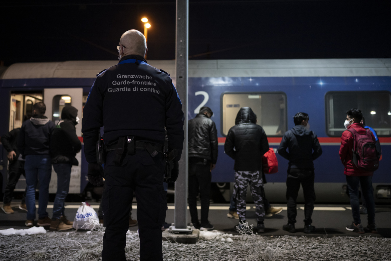 Migrantes observados por guarda de fronteira na estação de trens de Buchs station.