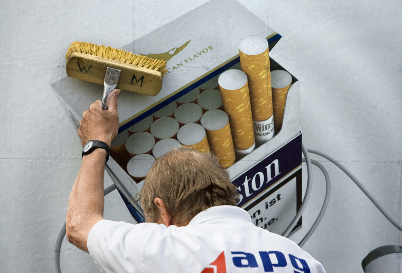 Un homme colle une affiche publicitaire pour le tabac