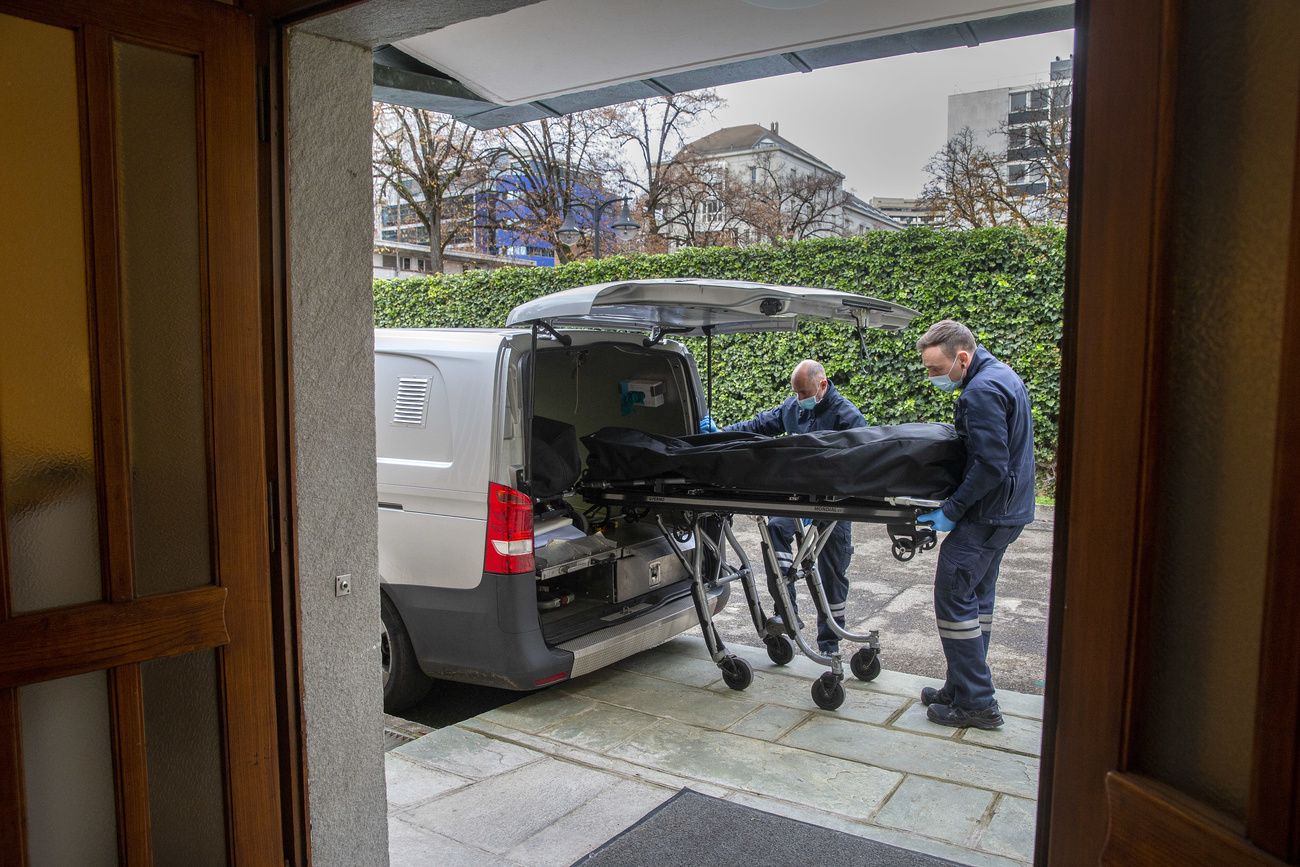 Funeral handlers carry body to car.